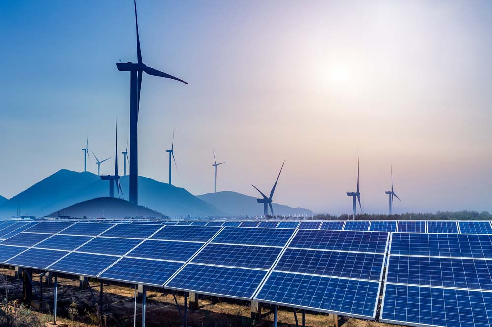 Sunlit solar panels in the foreground with wind turbines on distant hills, showcasing renewable energy landscape.