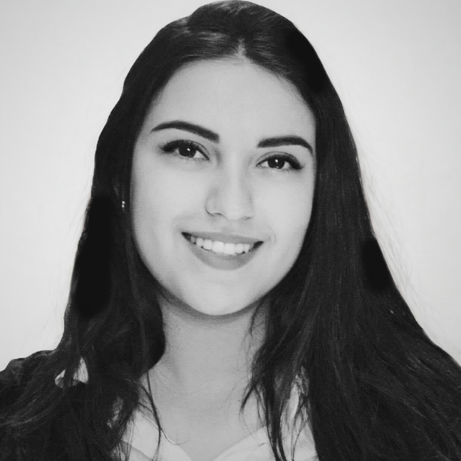 A black and white headshot of a person smiling, with dark wavy hair and wearing a collared shirt.