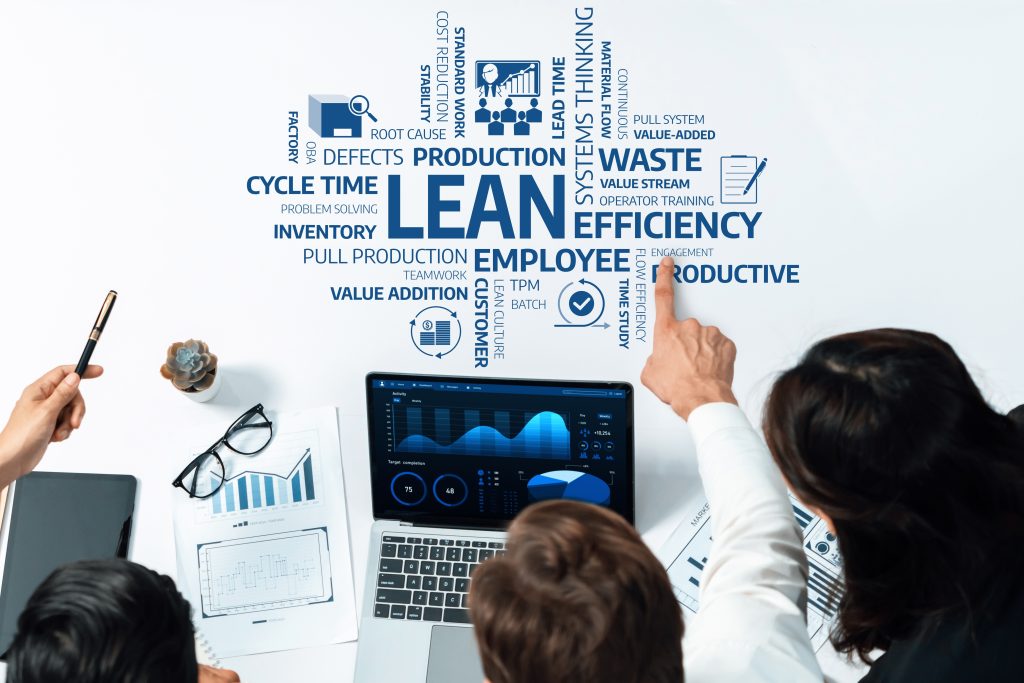 A team is looking at a laptop displaying business analytics with a word cloud about lean manufacturing principles in the background.